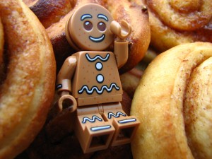 Lego Minifigur "Gingerbreadman" aus Sammelserie 11 liegt mit erhobenem Arm zwischen Zimtschnecken. noppenquader minifig moc