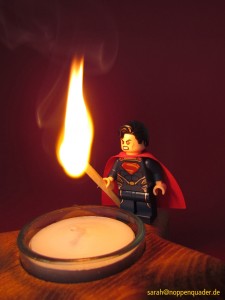 Lego Minifig Superman lights a match with his lasereyes in front of a christmans candle. Superman entzündet ein Streichholz mit seinem Laserblick vor einer Weihnachtskerze. noppenquader moc